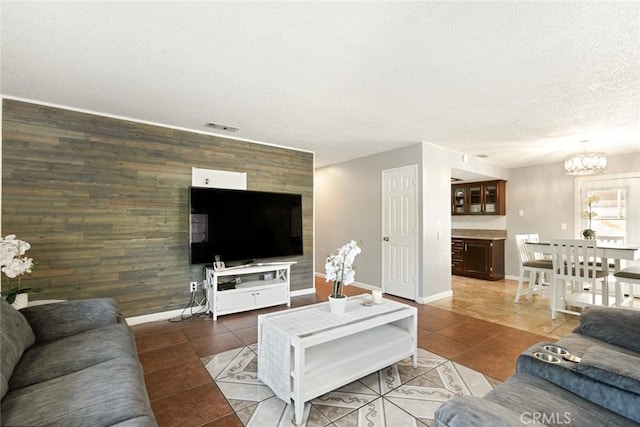 living room featuring a textured ceiling, an inviting chandelier, wood walls, and dark tile patterned floors