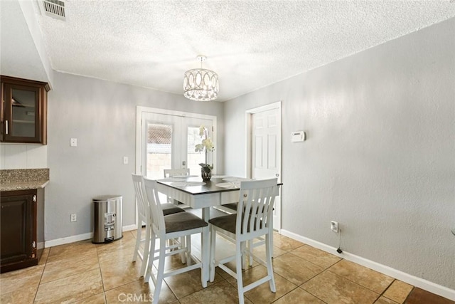 dining space featuring a textured ceiling, light tile patterned floors, french doors, and a notable chandelier