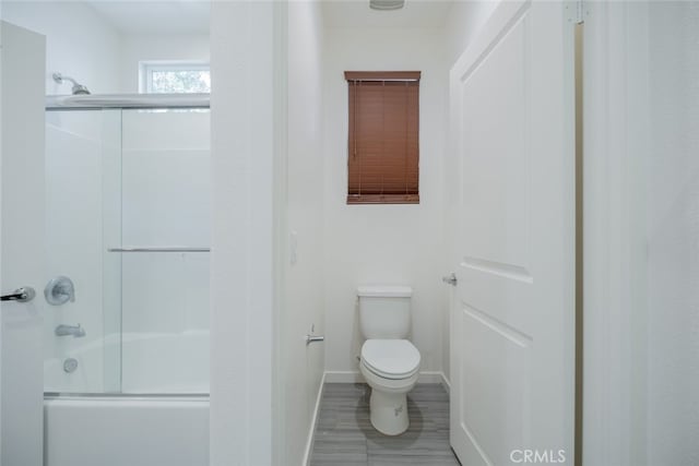 bathroom featuring toilet and bath / shower combo with glass door