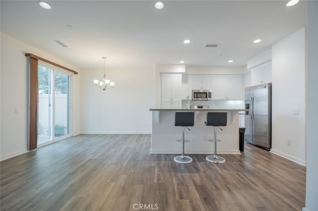 kitchen featuring white cabinets, appliances with stainless steel finishes, an inviting chandelier, hanging light fixtures, and hardwood / wood-style flooring