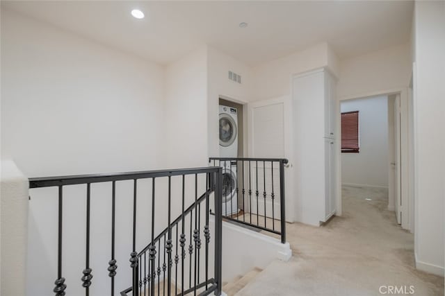 hall featuring light carpet and stacked washer / dryer