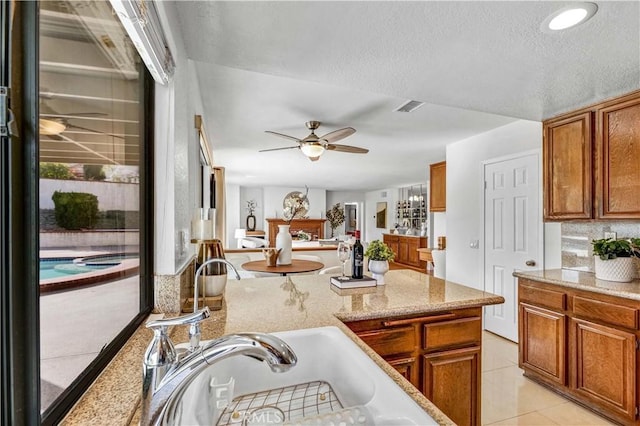 kitchen featuring ceiling fan, light tile patterned floors, light stone countertops, and sink