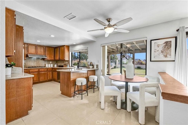 kitchen featuring a kitchen bar, black cooktop, tasteful backsplash, kitchen peninsula, and ceiling fan