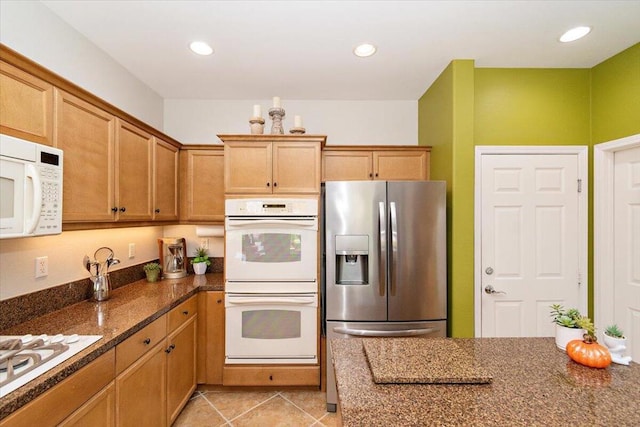 kitchen with white appliances, light tile patterned floors, and dark stone counters