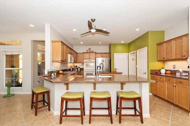 kitchen featuring ceiling fan, a kitchen breakfast bar, white appliances, and dark stone countertops