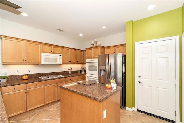 kitchen featuring white appliances, light tile patterned floors, dark stone counters, and a kitchen island