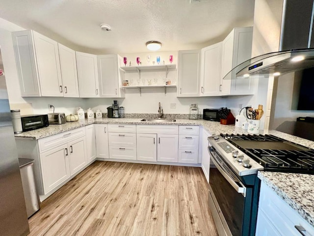 kitchen featuring stainless steel gas range, sink, white cabinets, and wall chimney range hood