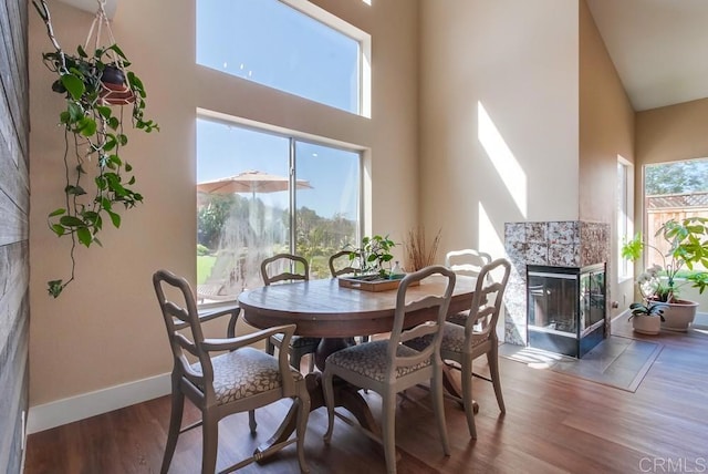 dining area with dark wood-type flooring, a healthy amount of sunlight, a fireplace, and a high ceiling