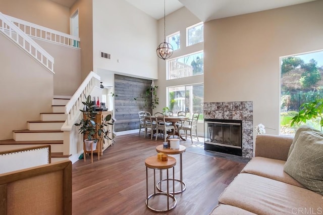 living room featuring plenty of natural light, a tiled fireplace, dark hardwood / wood-style flooring, and a high ceiling