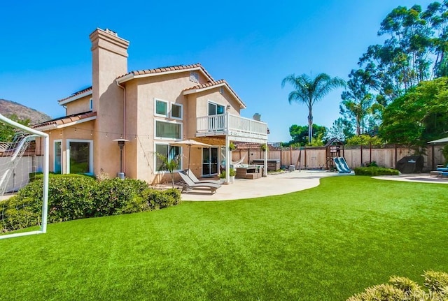 back of property featuring a playground, a yard, a balcony, and a patio