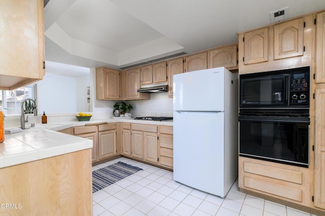 kitchen featuring light tile patterned floors, tile counters, a tray ceiling, light brown cabinetry, and black appliances