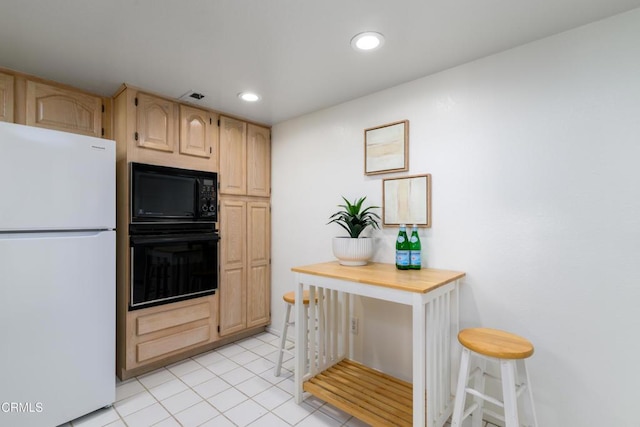 kitchen featuring light tile patterned flooring, light brown cabinetry, a breakfast bar, and black appliances