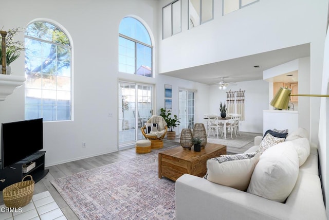 living room featuring ceiling fan, a high ceiling, and light wood-type flooring