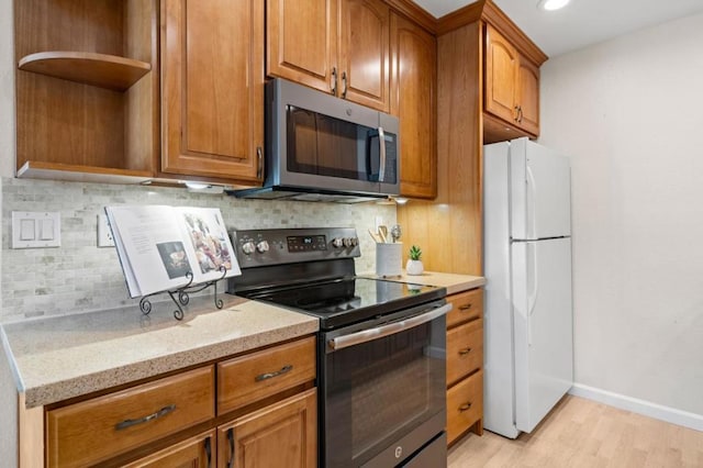 kitchen featuring backsplash, light stone countertops, stainless steel appliances, and light wood-type flooring