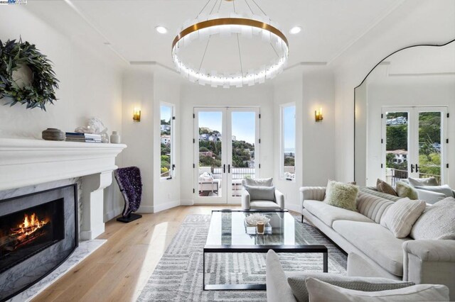 living room featuring light wood-type flooring, a high end fireplace, a healthy amount of sunlight, and french doors