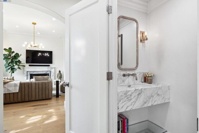 bathroom featuring hardwood / wood-style flooring, a premium fireplace, a chandelier, crown molding, and vanity