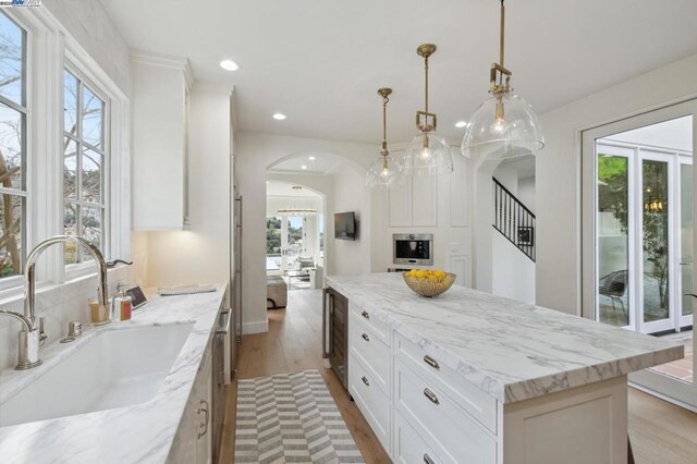 kitchen with a kitchen island, white cabinetry, sink, hanging light fixtures, and light stone counters