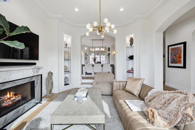 living room with built in features, a premium fireplace, ornamental molding, and a notable chandelier