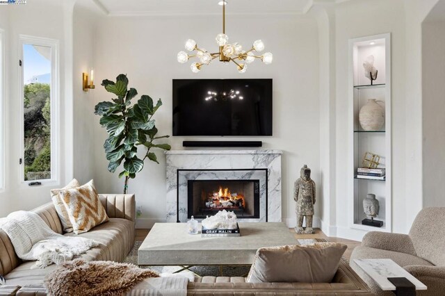 living room featuring built in features, plenty of natural light, a premium fireplace, and a chandelier