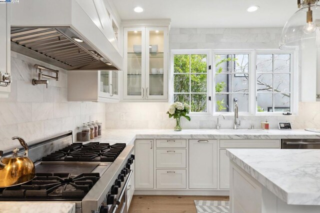 kitchen with white cabinetry, custom exhaust hood, appliances with stainless steel finishes, backsplash, and light stone countertops