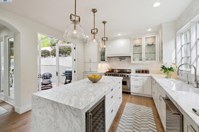 kitchen featuring beverage cooler, appliances with stainless steel finishes, a kitchen island, white cabinetry, and sink