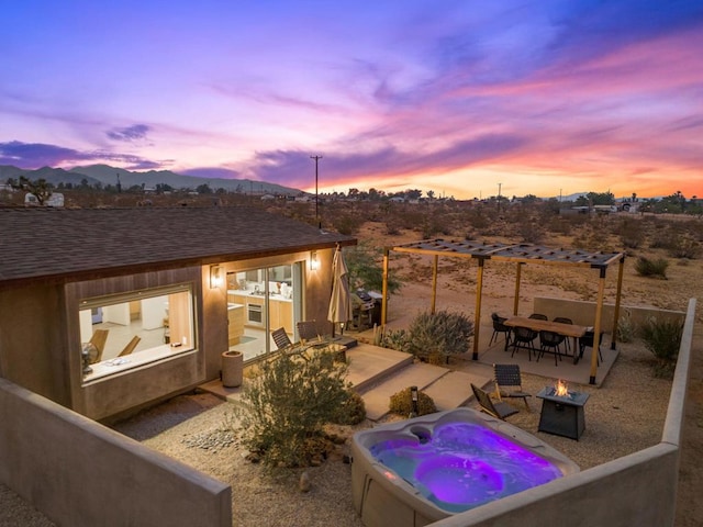 patio terrace at dusk featuring a mountain view, a hot tub, and a fire pit