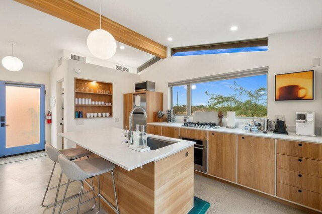 kitchen featuring a center island with sink, lofted ceiling with beams, sink, hanging light fixtures, and stainless steel appliances