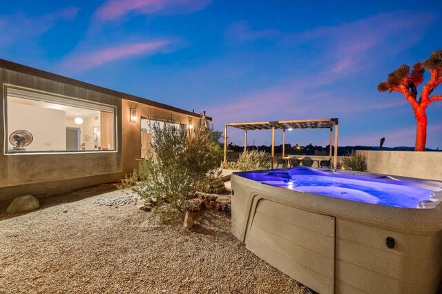 pool at dusk featuring a hot tub