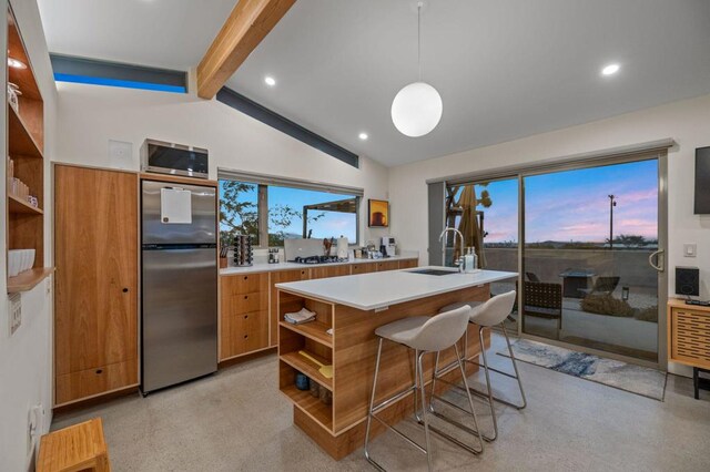 kitchen with pendant lighting, stainless steel appliances, sink, lofted ceiling with beams, and a center island with sink