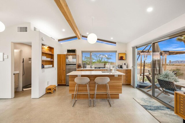 kitchen featuring decorative light fixtures, vaulted ceiling with beams, a healthy amount of sunlight, an island with sink, and stainless steel fridge