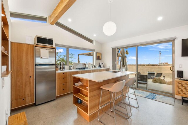 kitchen with pendant lighting, stainless steel appliances, vaulted ceiling with beams, sink, and a kitchen island with sink