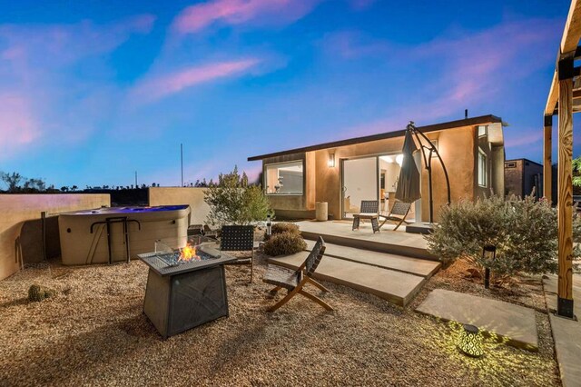 patio terrace at dusk featuring a hot tub and a fire pit