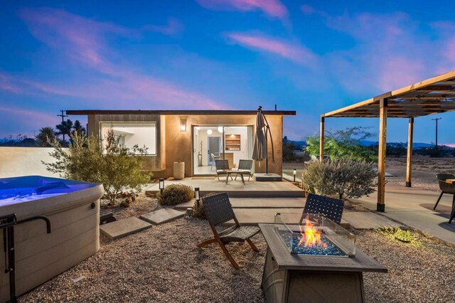 back house at dusk featuring a hot tub, a patio area, and a fire pit