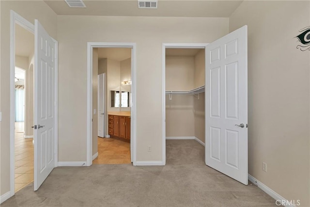 unfurnished bedroom featuring ensuite bath, light colored carpet, a closet, and a spacious closet