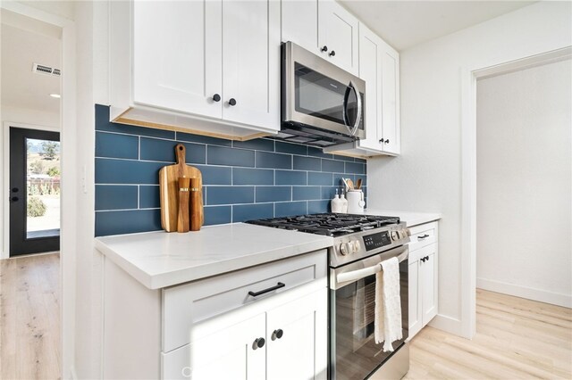 kitchen with light stone countertops, white cabinets, appliances with stainless steel finishes, and tasteful backsplash