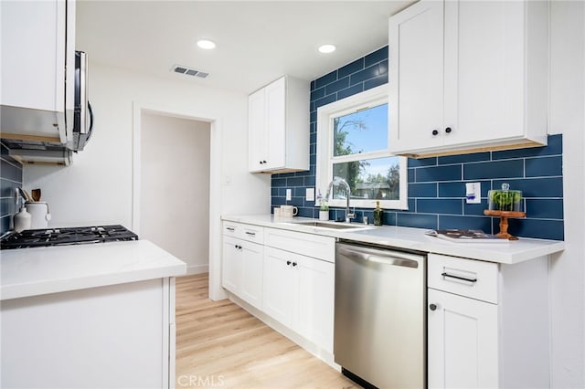 kitchen with white cabinetry, light hardwood / wood-style floors, stainless steel appliances, tasteful backsplash, and sink