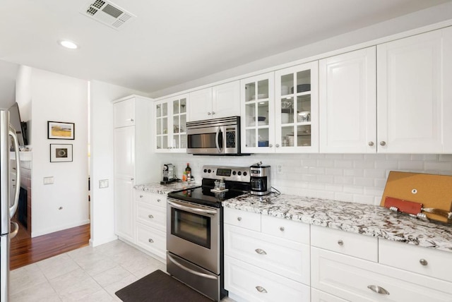 kitchen with light stone counters, light tile patterned floors, white cabinets, and stainless steel appliances