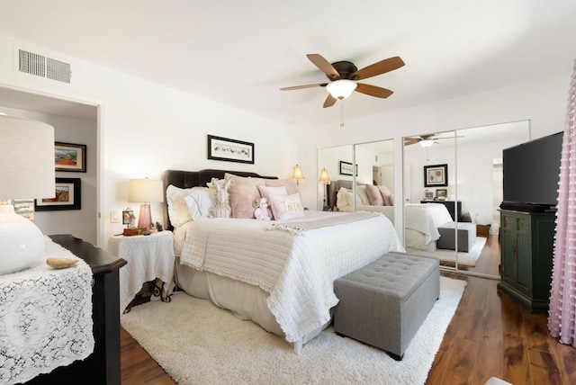 bedroom with dark wood-type flooring, ceiling fan, and two closets