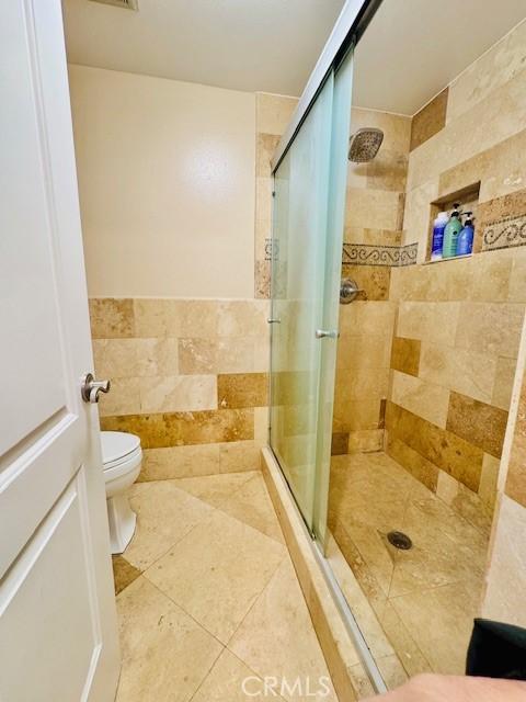 bathroom featuring an enclosed shower, toilet, and tile walls