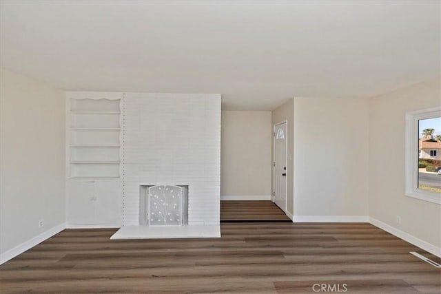 unfurnished living room with built in features, dark wood-type flooring, and a brick fireplace