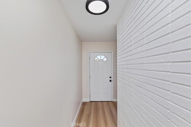 doorway to outside with light wood-type flooring and brick wall