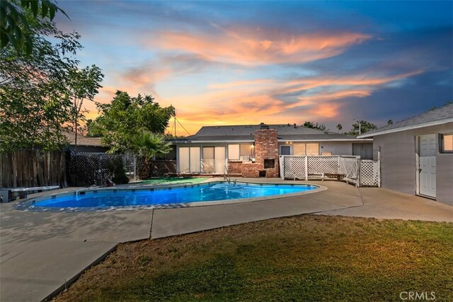 pool at dusk featuring a lawn and a patio