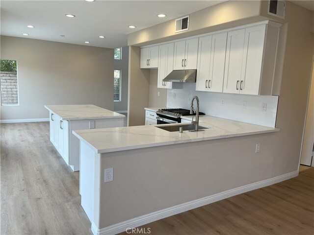 kitchen with light stone countertops, white cabinets, kitchen peninsula, and stainless steel range with gas stovetop