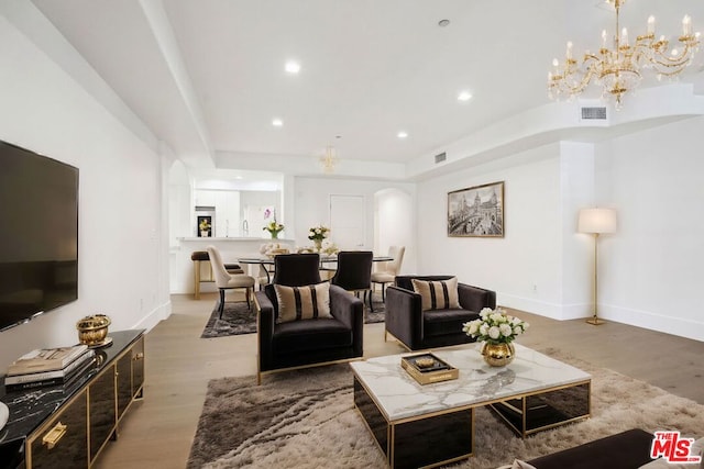 living room with a raised ceiling, wood-type flooring, and a notable chandelier