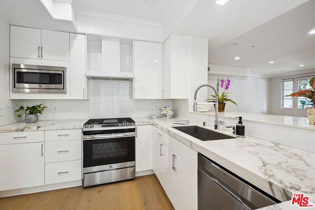 kitchen featuring range hood, stainless steel appliances, white cabinetry, and sink