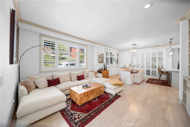 living room featuring a notable chandelier, crown molding, and light hardwood / wood-style floors