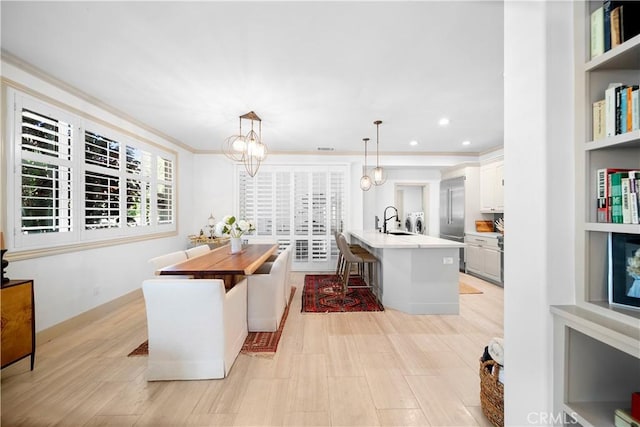 dining space featuring an inviting chandelier, light hardwood / wood-style floors, sink, crown molding, and built in shelves