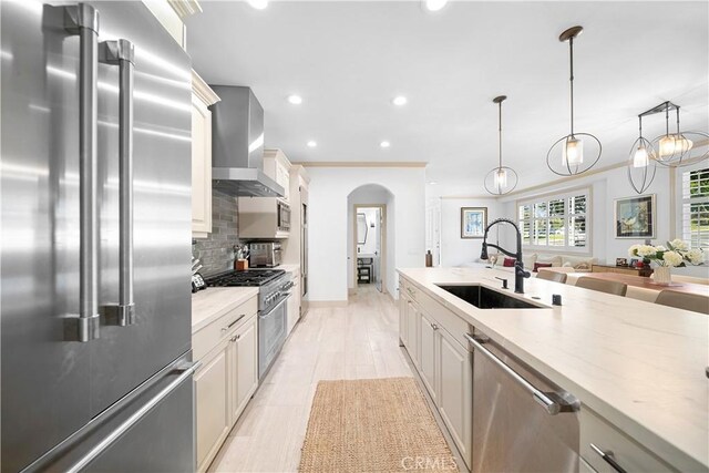 kitchen with tasteful backsplash, hanging light fixtures, high end appliances, wall chimney exhaust hood, and sink