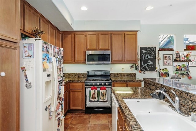 kitchen with appliances with stainless steel finishes, sink, dark tile patterned flooring, and dark stone counters