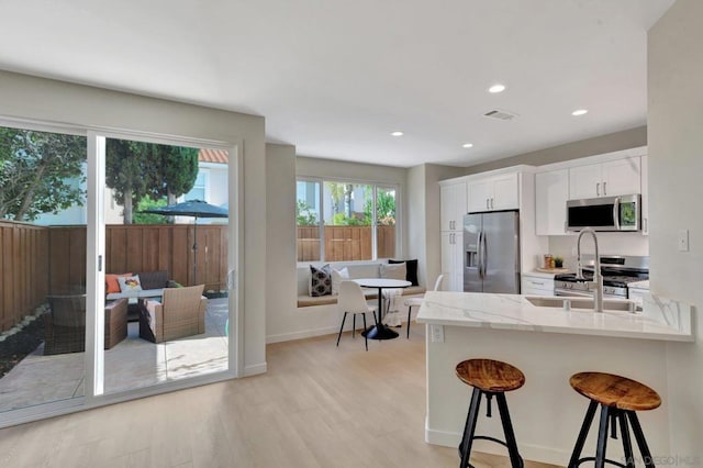 kitchen featuring a kitchen bar, appliances with stainless steel finishes, light stone counters, light hardwood / wood-style flooring, and white cabinets